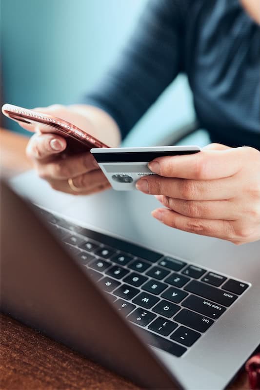 Person holding a credit card over a laptop keyboard.